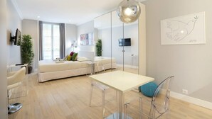 Een moderne woonkamer met een bank, een eettafel en stoelen. Er is een tv aan de muur bevestigd en een plant in de hoek.