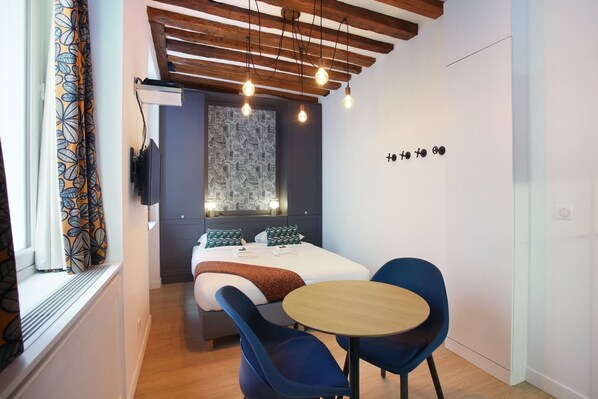 A bedroom with a bed, a round table, two chairs, a TV, and a patterned curtain. - Cadet 101 - Studio Apartment, Sleeps 2 (Paris)
