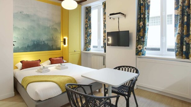Une chambre d’hôtel avec un lit, une table, des chaises, une télévision et un tableau au mur.