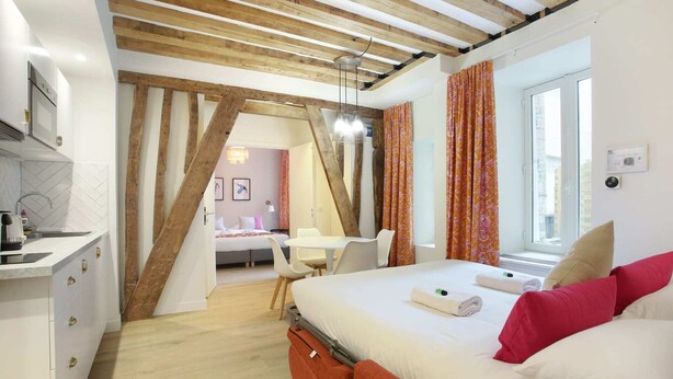 A modern bedroom with a wooden ceiling, a bed with white and red bedding, a desk, and a chair.