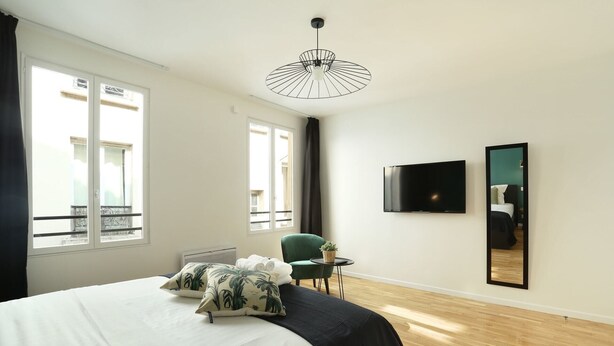 Quarto de hotel com cama, cadeira, mesa pequena, televisão e uma janela grande.