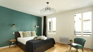 Quarto moderno com cama, uma cadeira e uma mesinha.