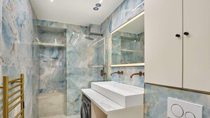 A bathroom with a marble wall, a sink, a mirror, a shower, and a washing machine. - Caire 3 - One Bedroom Apartment, Sleeps 6 (Paris)