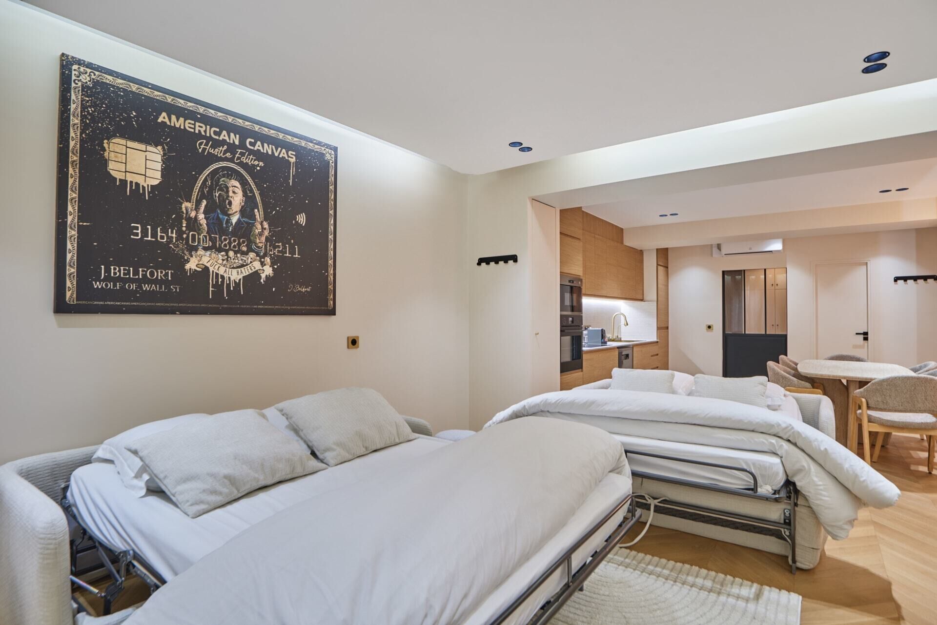 Une chambre d’hôtel avec deux lits, une kitchenette, un coin repas et une grande œuvre d’art imprimée sur toile accrochée au mur.