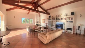 Amplia sala de estar con techo alto, piso de baldosas y chimenea. Hay un sofá, una mesa de centro y una estantería llena de libros y adornos.