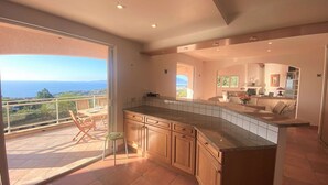 Una cocina moderna con una isla grande, armarios de madera y vista al mar a través de un gran ventanal corredero.