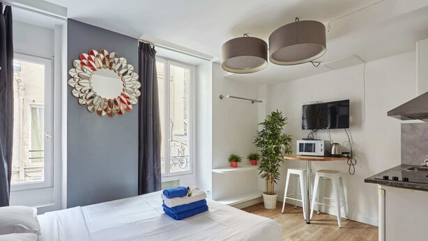 A modern hotel room with a bed, a desk with a TV, a microwave, and a plant. - Caire 5 - Studio Apartment, Sleeps 2 (Paris)