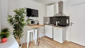 A compact kitchen with a microwave, toaster, and stove. There are two white stools and a potted plant. - Caire 5 - Studio Apartment, Sleeps 2 (Paris)