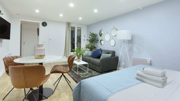 Moderni hotellihuone, jossa on sänky, sohva, ruokapöytä tuoleineen, pieni sohvapöytä ja lamppu.