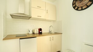 A compact kitchen with white cabinetry, a stainless steel sink, a built-in range hood, and a wall clock. - Charon 2 - Studio Apartment, Sleeps 2 (Paris)