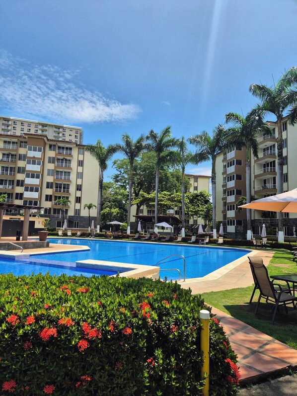 A swimming pool surrounded by palm trees and a building with balconies.
