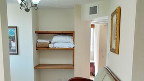 Una stanza con un divano rosso, uno scaffale in legno con asciugamani piegati, una lampada a soffitto e un quadro appeso al muro.
