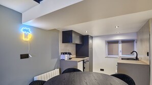 A modern kitchen with dark cabinets, a built-in oven, and a window with blinds. - Chenier appart - Studio Apartment, Sleeps 4 (Paris)