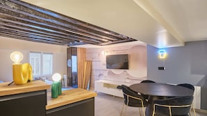 A modern living room with a wooden ceiling, a flat-screen TV mounted on the wall, a round dining table with black chairs, and a neon sign on the wall. - Chenier appart - Studio Apartment, Sleeps 4 (Paris)