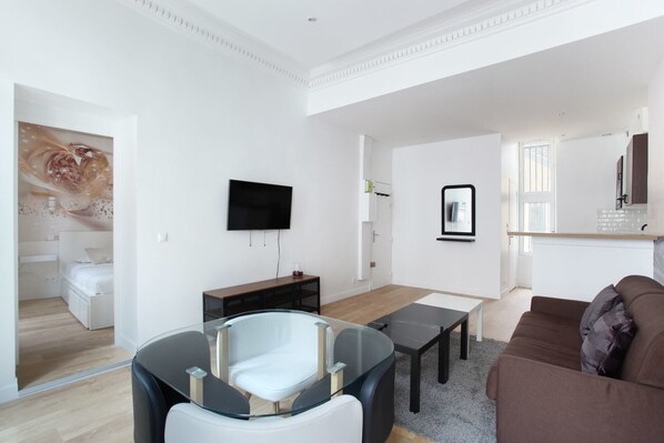 A modern living room with a flat-screen TV, a glass dining table, and a brown sofa.