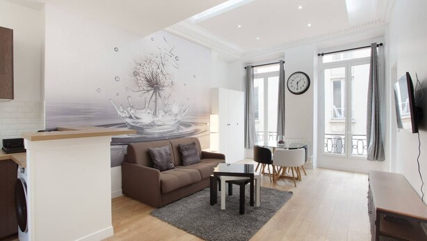 A modern living room with a brown sofa, a glass coffee table, and a dining area with a white table and chairs.