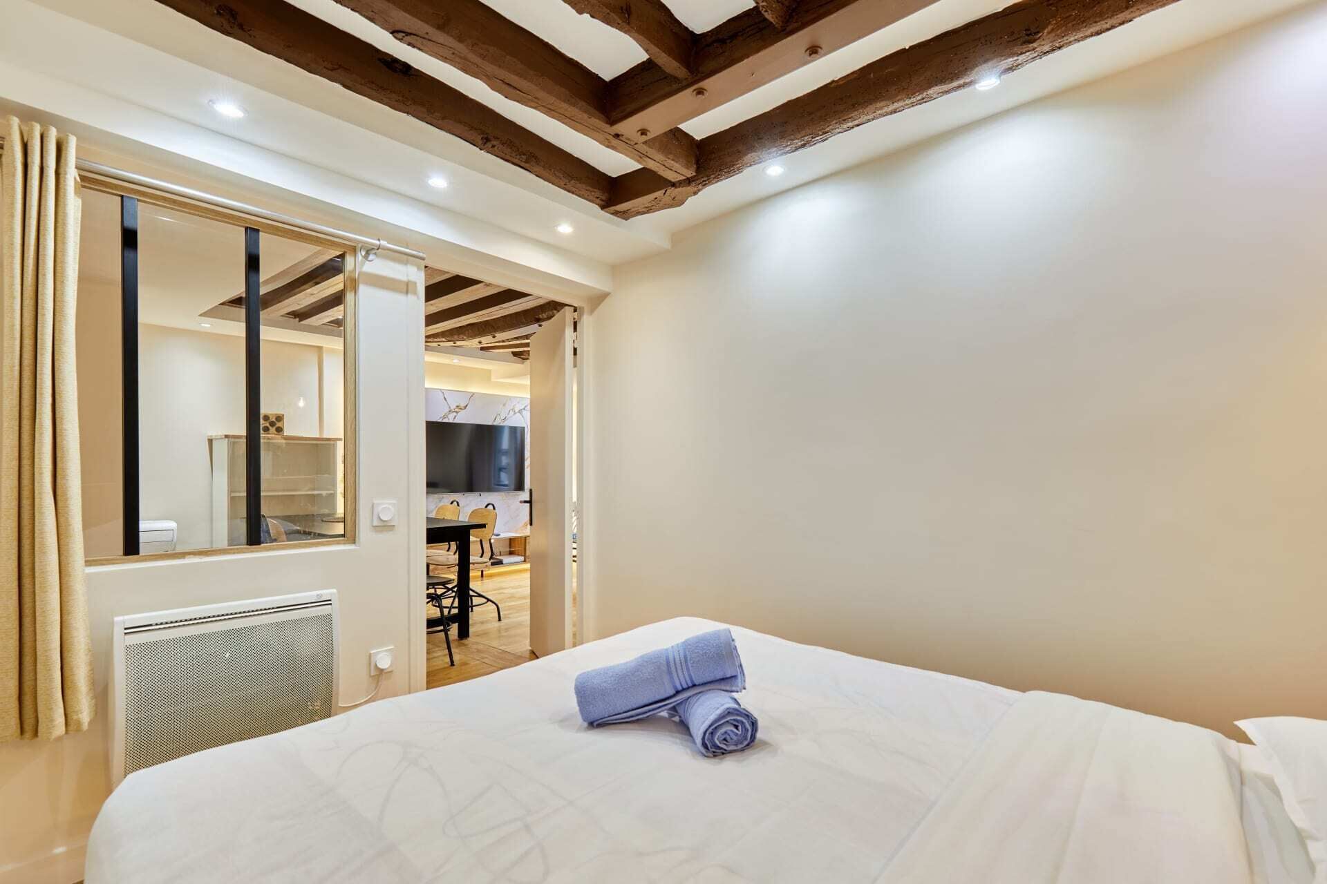 A hotel room with a bed, a bathroom, and a dining area visible through an open door.