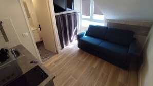 A compact living space with a kitchenette, a sofa, and a TV mounted on the wall. - Cosy Studio - Studio Apartment, Sleeps 2 (Paris)
