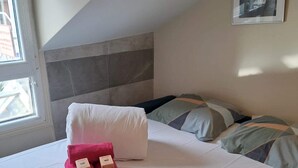 A neatly made bed with a white mattress and a headboard with a gray and white pattern. There are two rolled pink towels with tags on the bed. - Cosy Studio - Studio Apartment, Sleeps 2 (Paris)