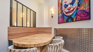 Ein Essbereich mit einem runden Holztisch und gepolsterten Stühlen, einem großen, farbenfrohen Gemälde an der Wand und einer gemusterten Wand hinter der Sitzgruppe.