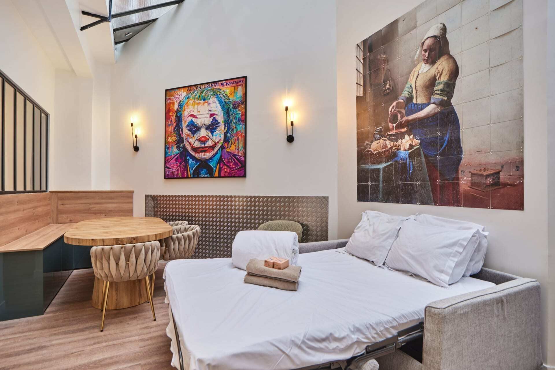 Een hotelkamer met een bed, een ronde houten tafel, twee stoelen, een hoofdbord en twee wandlampen.