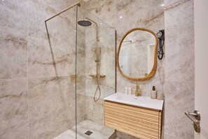 Un baño con ducha de vidrio, tocador de madera con lavamanos y un espejo grande.