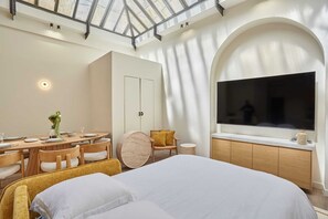 Una habitación de hotel moderna con cama, una mesa de comedor, sillas, televisión y tragaluz.