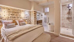 A bedroom with a stone wall, a bed, a bathroom with a shower, and a small kitchen area. - Meslay 3 - Two Bedroom Apartment, Sleeps 6 (Paris)