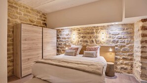 A bedroom with a stone wall, a bed with a wooden headboard, and a wooden wardrobe. - Meslay 3 - Two Bedroom Apartment, Sleeps 6 (Paris)