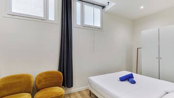 A bedroom with a bed, two chairs, a wardrobe, and a window with curtains.