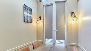 Un espace repas avec une table en bois et des chaises en cuir, une porte dotée d’un panneau en verre dépoli et des lampes fixées au mur.