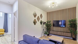 Un salon moderne avec un canapé gris, un téléviseur à écran plat fixé sur un mur recouvert de panneaux en bois et des miroirs décoratifs.