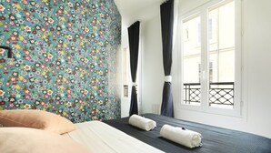 A hotel room with a bed, a window with curtains, and a floral-patterned wall. - Meslay 8 - Studio Apartment, Sleeps 2 (Paris)