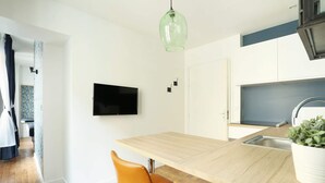 A modern kitchen with a wooden island, a flat-screen TV, and a hanging light fixture. - Meslay 8 - Studio Apartment, Sleeps 2 (Paris)