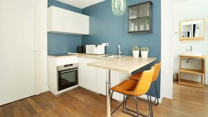 A compact kitchen with a built-in oven, a microwave, and a sink. There is a bar stool and a potted plant on the counter. - Meslay 8 - Studio Apartment, Sleeps 2 (Paris)