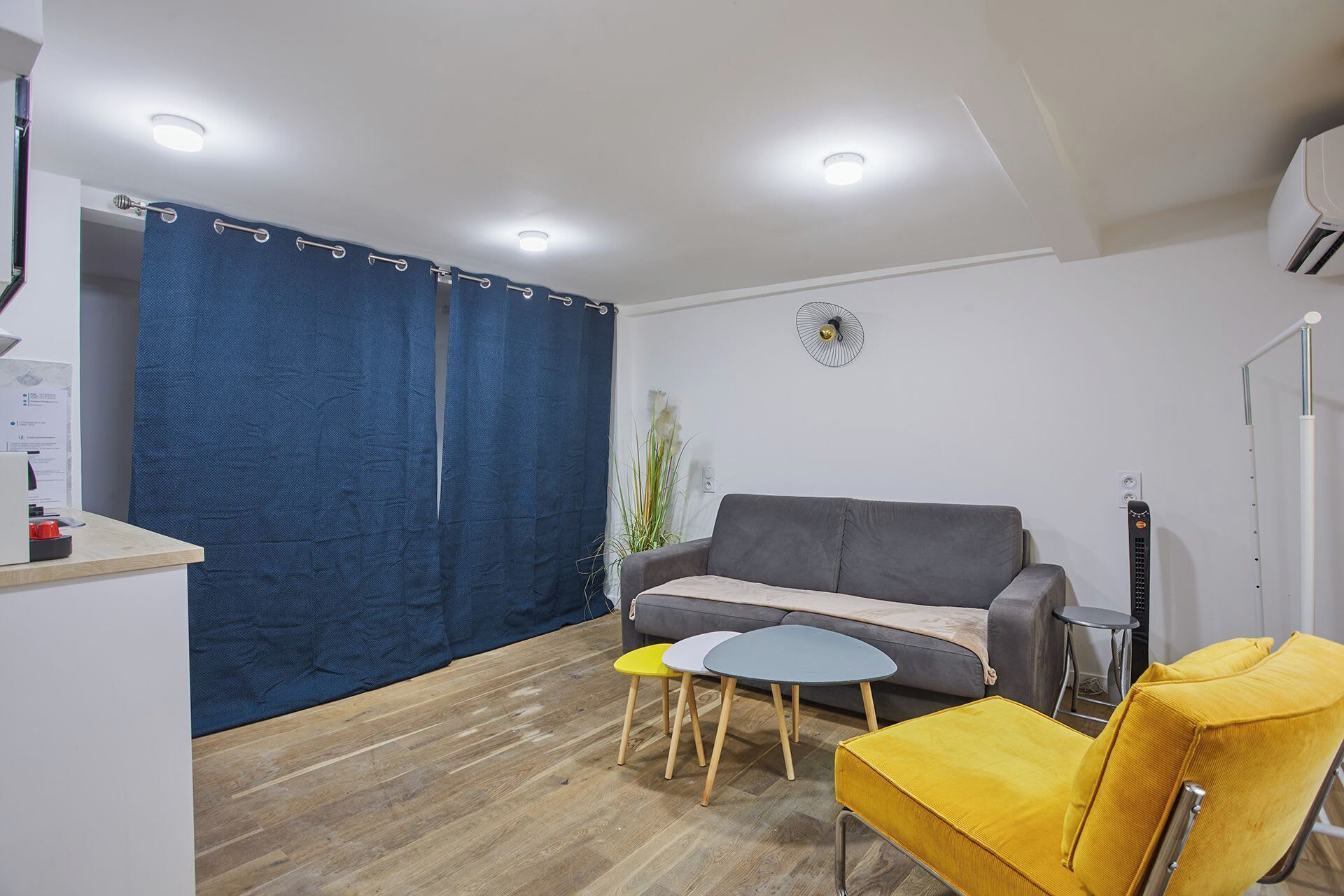 A compact living space with a grey sofa, a yellow chair, a small round table, and a blue curtain.