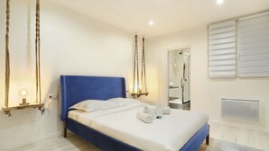 Un dormitorio con cabecera azul, cama con sábanas blancas, una hamaca colgante, ducha de vidrio y un radiador.
