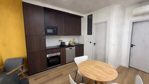 A compact kitchen with dark wooden cabinets, a microwave, and a dishwasher. There is a round wooden table with four white chairs in the dining area. - St Denis 2 - One Bedroom Apartment, Sleeps 6 (Paris)