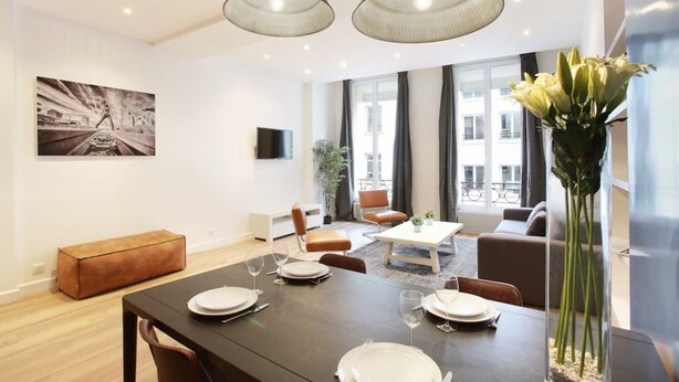 Un salon moderne comprenant un coin repas, de grandes fenêtres, un téléviseur à écran plat et un tableau accroché au mur.