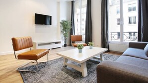 Un salon moderne avec un canapé, un fauteuil, une table basse et un téléviseur fixé au mur.
