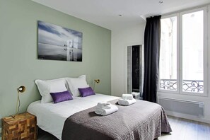 Una habitación de hotel con cama, un cuadro, una ventana con vistas y una mesita de noche.