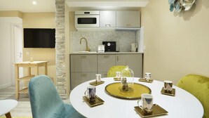 A modern dining area with a round table set for four, a kitchen with a microwave and toaster, and a stone accent wall. - St Honore - Two Bedroom Apartment, Sleeps 6 (Paris)