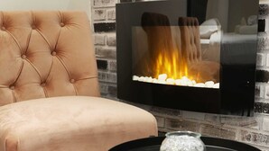 A tufted armchair, a television with a fireplace display, a small round table with a decorative bowl, and a fluffy rug. - St Honore - Two Bedroom Apartment, Sleeps 6 (Paris)
