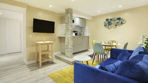 A modern living room with a blue sofa, a small wooden table, and a kitchen area with a stone pillar. - St Honore - Two Bedroom Apartment, Sleeps 6 (Paris)