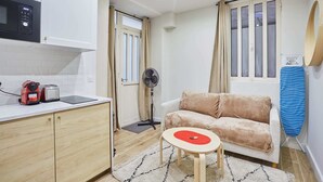 A compact living space with a kitchenette, a sofa, a small table, and a fan.