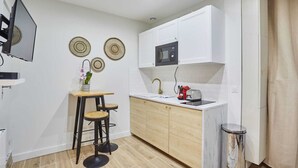 A compact kitchen with white cabinets, a wooden countertop, a sink with a gold faucet, and a small trash bin.