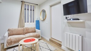 A modern living room with a beige sofa, a small round table, a mounted TV, and a white radiator.