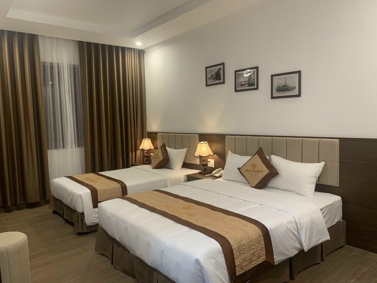 Een hotelkamer met twee bedden, een groot raam met gordijnen, en drie ingelijste foto’s aan de muur.