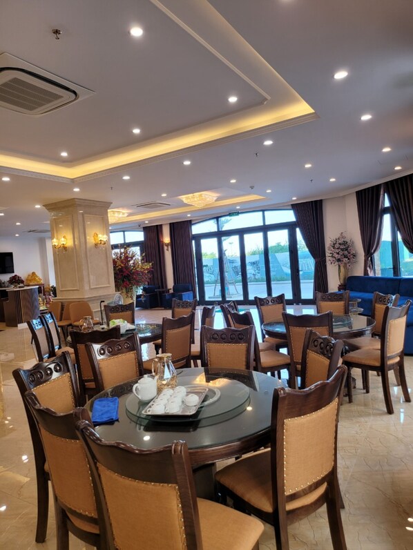 A spacious dining area with round tables and chairs, large windows, and a chandelier. - ViNH KHANG HA LONG HOTEL (Bai Chay)