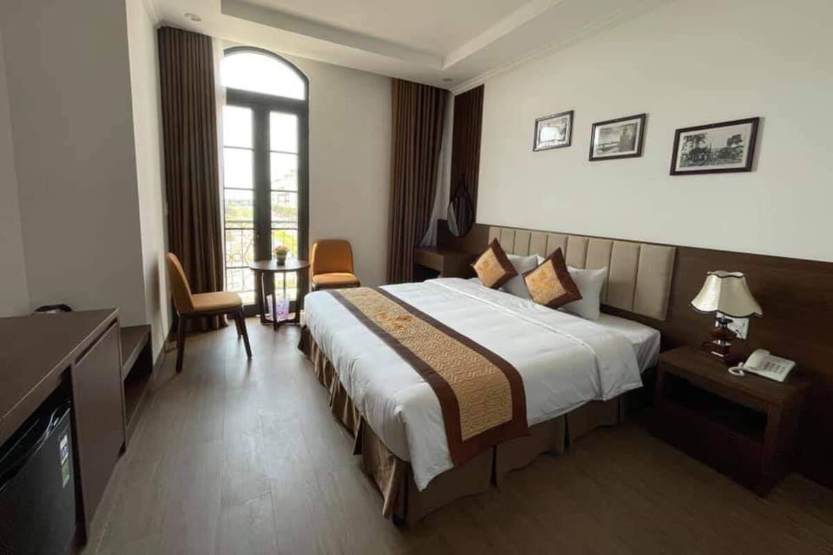 A hotel room with a large bed, a desk, a chair, a small table, and a window with curtains.